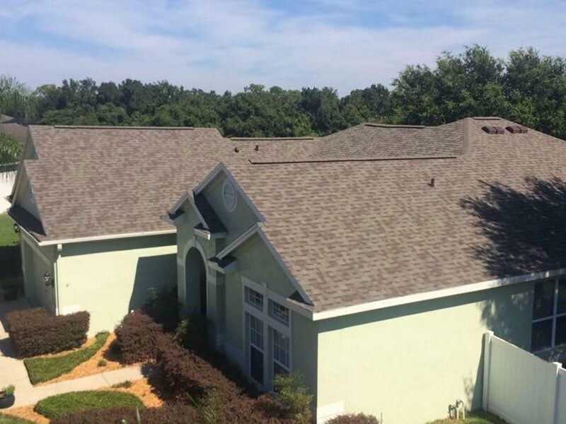 A green home with light brown asphalt shingles.