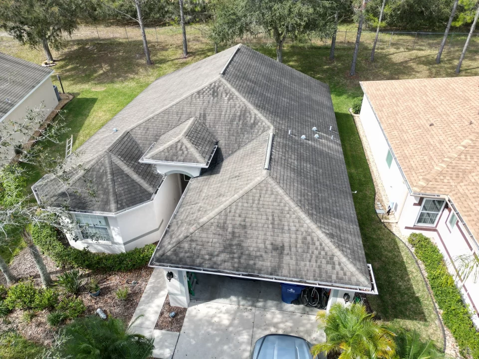 Drone shot of a suburban home featuring a grey tiled roof with surrounding greenery before roof replacement.